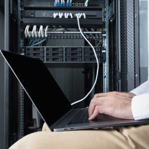 Close up of engineer in beige pant and white shirt, sitting in front of control panel, typing at laptop in hand, follow up his routine daily checking